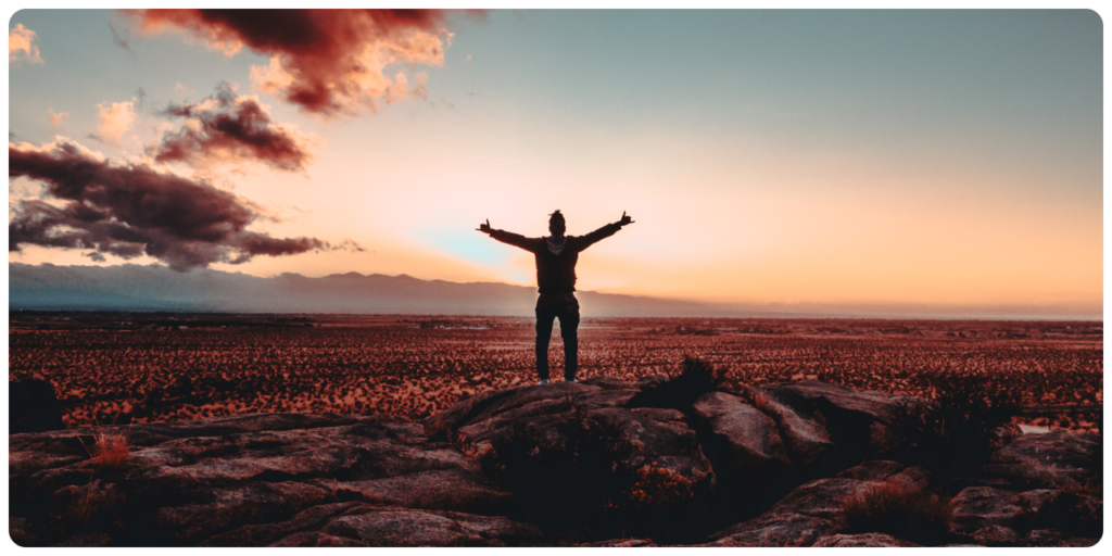 A man embracing mental health while standing on top of a rock with his arms outstretched.