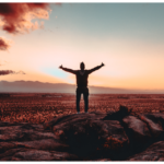 A man embracing mental health while standing on top of a rock with his arms outstretched.