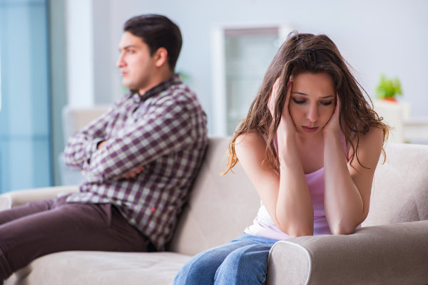 A man and woman experiencing mental health challenges sit on a couch with their hands on their heads.