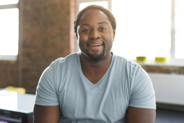 A black man displaying mental health in an office with a smile on his face.