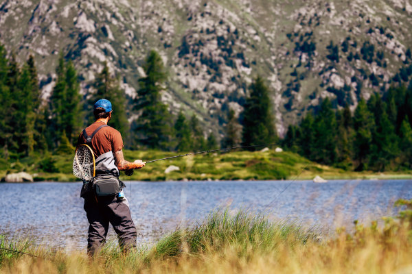 A man is standing in front of a serene lake with mountains in the background, contemplating his mental health.