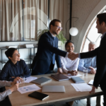 Five business professionals gathered around a conference table, two men in suits shaking hands while three others, two women and a man, observe and smile. Their discussion highlighted employer benefits, specifically the implementation of an Employment Assistance Program to provide mental health supports.