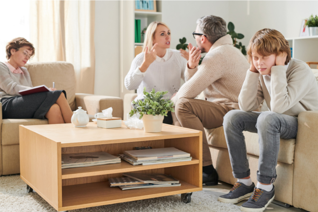 A family therapy session showing a couple arguing, a therapist observing and taking notes, and a child covering their ears, sitting nearby—the perfect setting for effective divorce counseling.