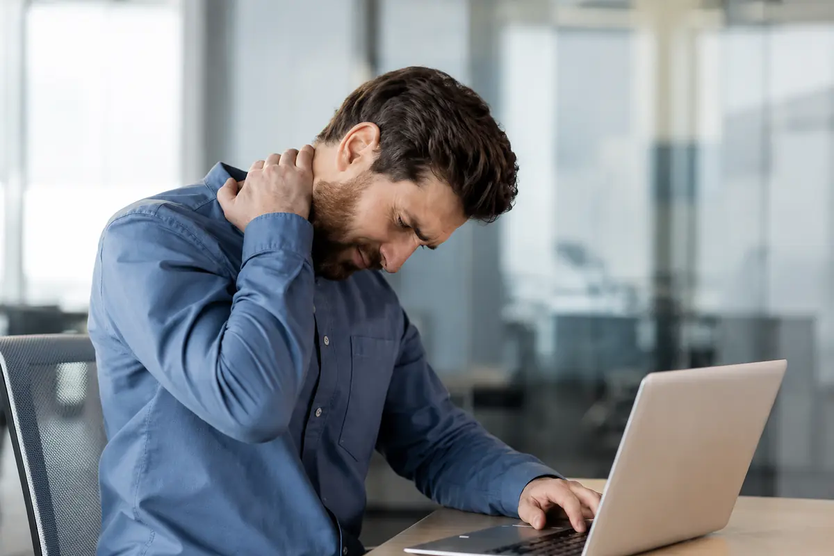 Office worker experiencing neck pain while working at a laptop